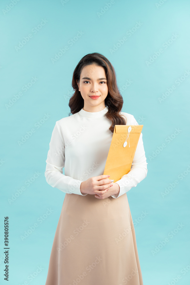 Smart looking woman in casual clothes holding a big enveloper over light blue background Smart looking woman in casual clothes holding a big enveloper over light blue background