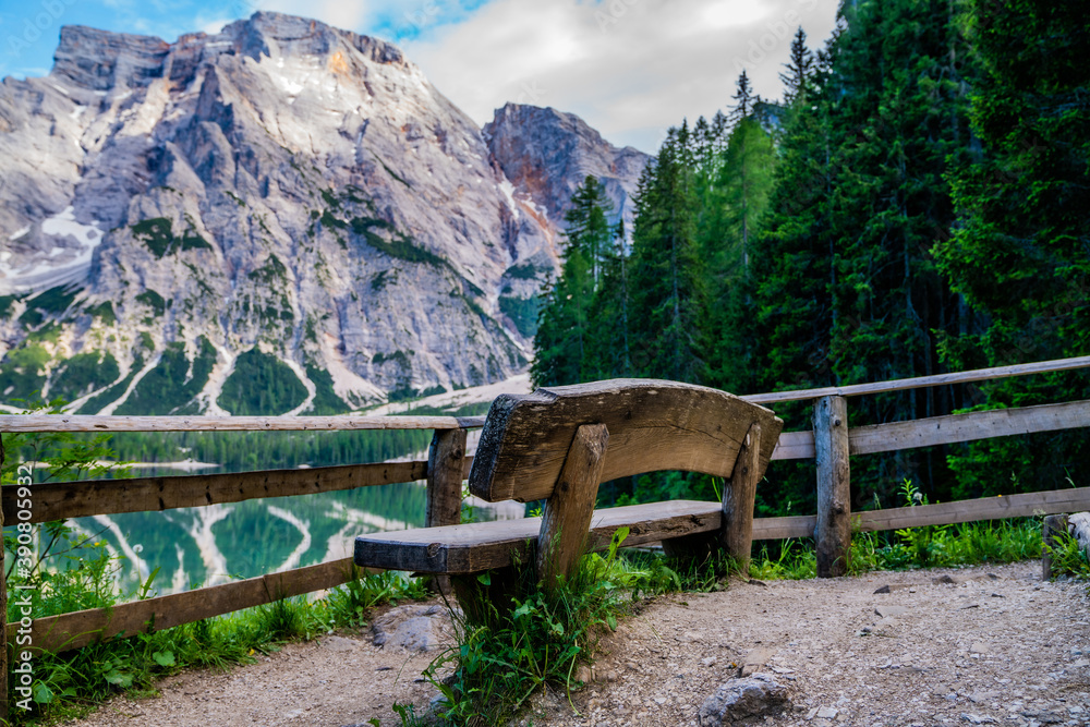 Wooden bench at the bank of famous and very popular travel destination lake Braies. South Tyrol in Italy, Europe. Spring or summer season, green leaves trees at background.