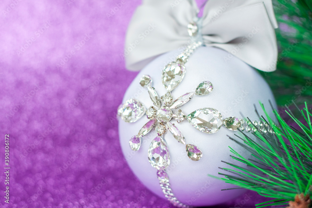 White Christmas ball in rhinestones for Christmas tree decoration. Christmas toy. Christmas toy for decorating a Christmas tree on a lilac background. Shining crystals on a white ball.