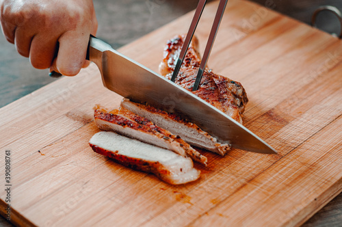 Chef hand with knife cutting meat on wooden board photo