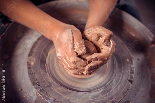 The potter's hands are shaped a cup from a clay. The process of creating pottery on a potter's wheel. The master ceramist works in his studio. Close-up, only hands. Crockery from clay own hands. photo