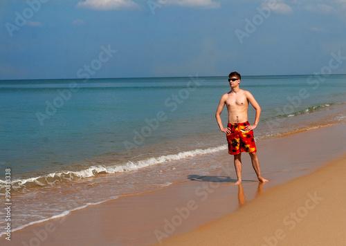 A young man stands on the sand on the shores of Andamand Bay in Phuket in shorts and sunbathes. photo