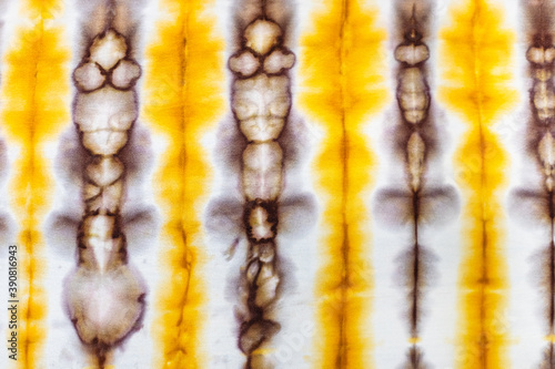 textile background - abstract spotted yellow and brown decor in tie-dye batik technique on white silk fabric of handcrafted scarf
