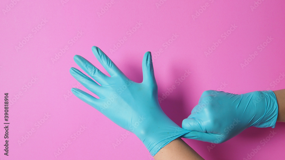 Hand is pulling blue latex gloves on pink background. Hand is pulling blue latex gloves on pink background.
