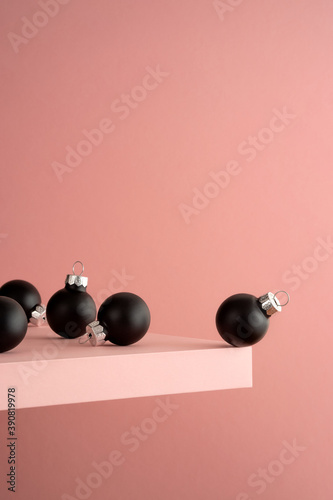 Several black Christmas balls on the pink shelf at the edge of the cliff. Pink background. Before the jump.