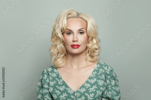Elegant woman with makeup and blonde curly hair on light green background