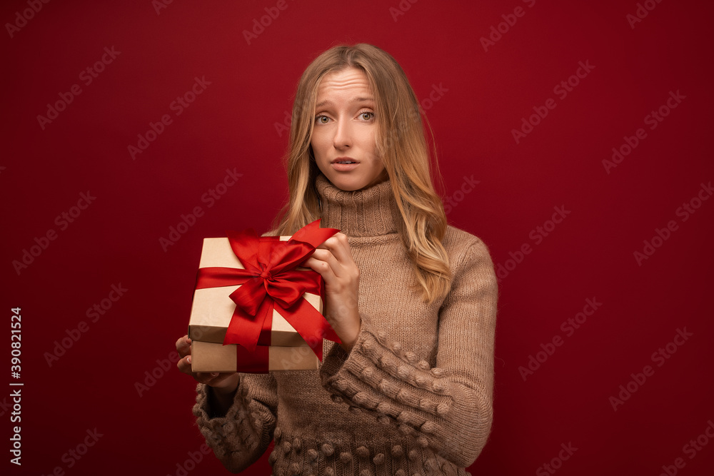 Charming blonde woman open a gift with red ribbon. Studio shot red background. New Year Birthday Holiday concept Charming blonde woman open a gift with red ribbon. Studio shot red background. New Year Birthday Holiday concept