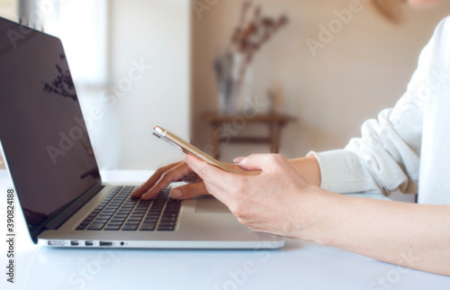 スマートフォンを見ながらノートパソコンを操作する女性