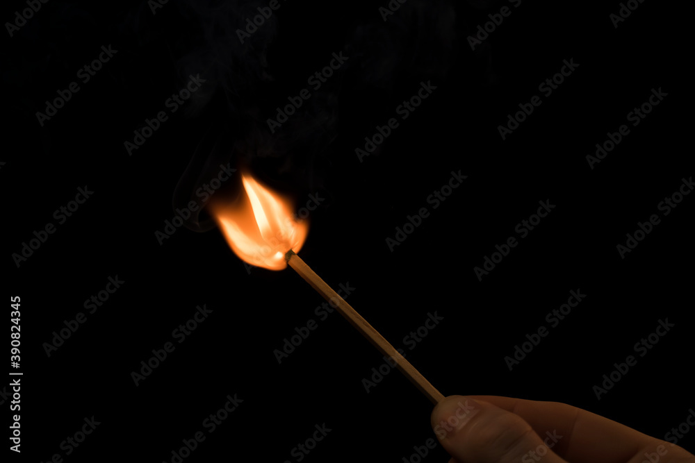 A lighted match on a black background. Hold a lighted match. The fire from the match illuminates everything around. Arson, danger, flash. Macro fire burning on matchstick. Idea, concept,