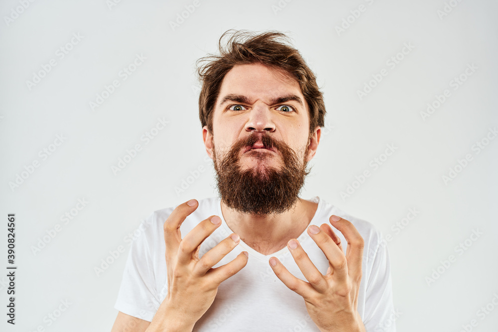 Emotional bearded man in a white t-shirt gestures with his hands light background Emotional bearded man in a white t-shirt gestures with his hands light background