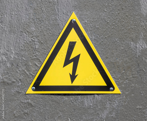 yellow triangle danger sign with lightning bolt on a gray wall, electricity attension mark of high voltage close up, dangerous place for riskly electric