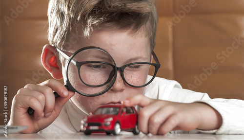 Child boy with magnifying glass inspecting red toy car. Concept of choice. Magnifier helps expert to estimate the benefits. How to choose transport