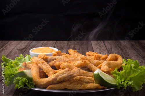 Breaded fried fish served on lettuce leaves with lemons and tartar sauce to accompany. Hot with smoke. Close-up photography. photo