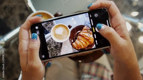 Close up of woman holds modern smartphone and taking pictures of her morning breakfast coffee and tasty croissant buns to share photos on social media resources