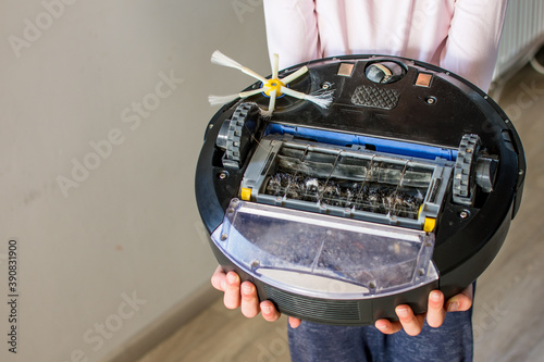 Robotic vacuum clener upside down with dust, trash and hair in human hands. Smart cleaning concept. photo