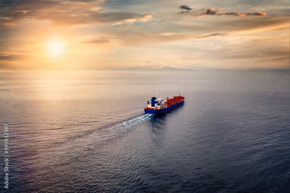 Aerial view of a container cargo ship sailing over calm sea into the sunset