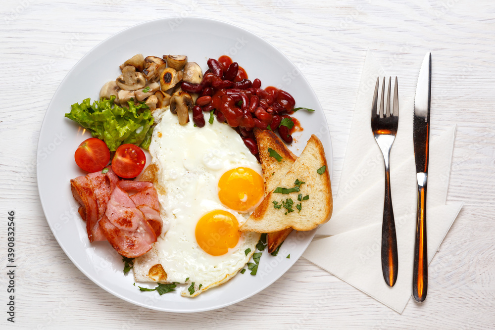 English Breakfast, fried eggs, ham, mushrooms on a white plate with a knife and fork English Breakfast, fried eggs, ham, mushrooms on a white plate with a knife and fork