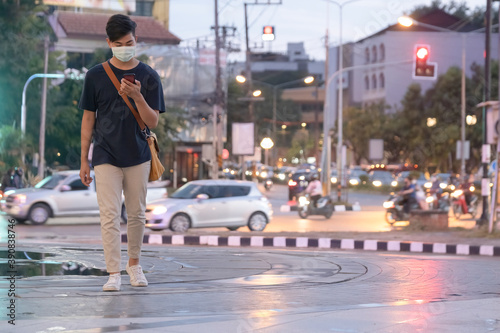 Young man with protective face mask using mobile phone in city street.