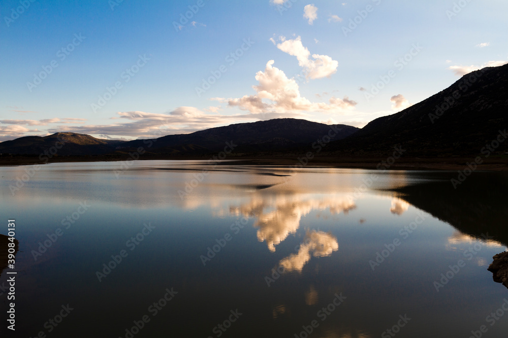 Artificial lake Mornos, Lidoriki Greece. The clouds are reflecting in the water. The mountains as a silhouette reflecting in the water too. Deep blue, black and white colors. Artificial lake Mornos, Lidoriki Greece. The clouds are reflecting in the water. The mountains as a silhouette reflecting in the water too. Deep blue, black and white colors.