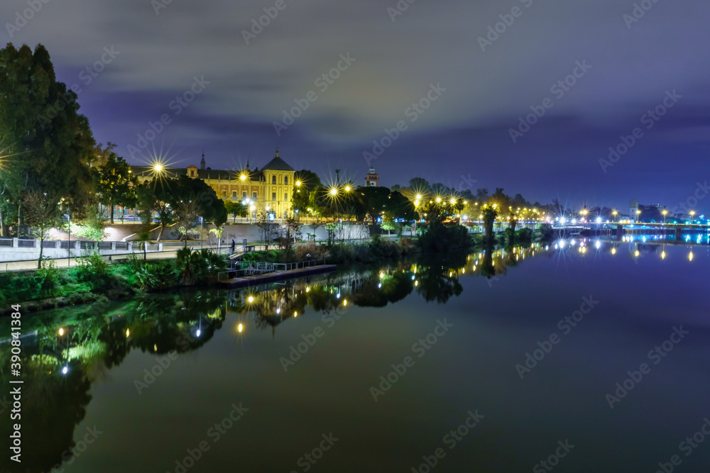 Río Guadalquir en Sevilla, puente sobre el río con edificios al fondo iluminados en una noche lluviosa de invierno.