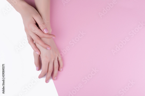 Beautiful women s hands with a stylish pink manicure on a pink and white background.