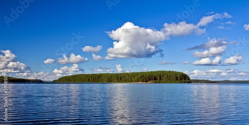 An island covered with thick forest in the river against blue sky with clouds in Kenozersky National Park, Arkhangelsk region, Russia.