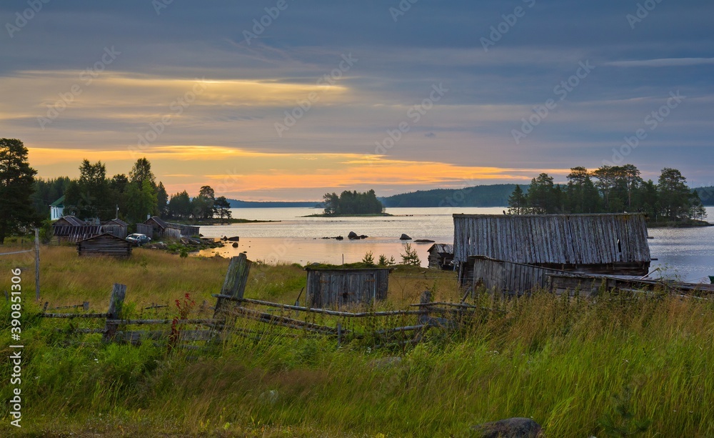 Rural area in summer in North Karelia, Russia. Small wooden houses on the bank of the White sea against colorful sunset.