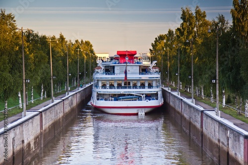 A ferry ship full of passengers in the lock of Volga-Baltic Canal and growing trees along it in Vytegra, Vologda Oblast, Russia. photo