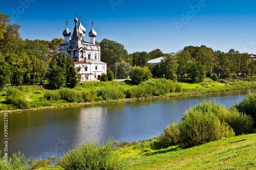 White orthodox Church of St. John of Chrysostom among green tall trees on the bank of the river in Vologda, Russia.