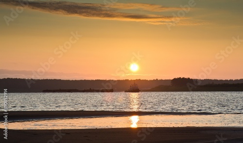 The view on sunset at the beach of the Northern Dvina river  a ship and a barge floating  and forests in the background in Russia.