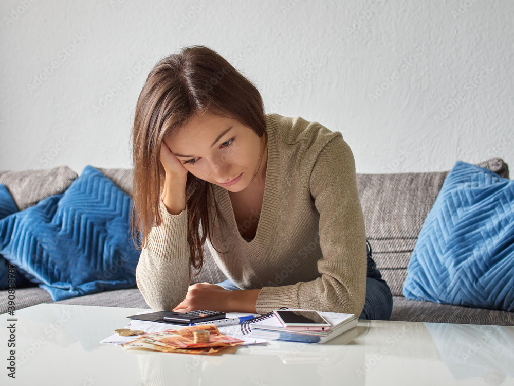 A young, depressed, stressed woman props her head with her hand. Pensive, broken and sad girl bends over the bills. There is euro money and a calculator on the table A young, depressed, stressed woman props her head with her hand. Pensive, broken and sad girl bends over the bills. There is euro money and a calculator on the table