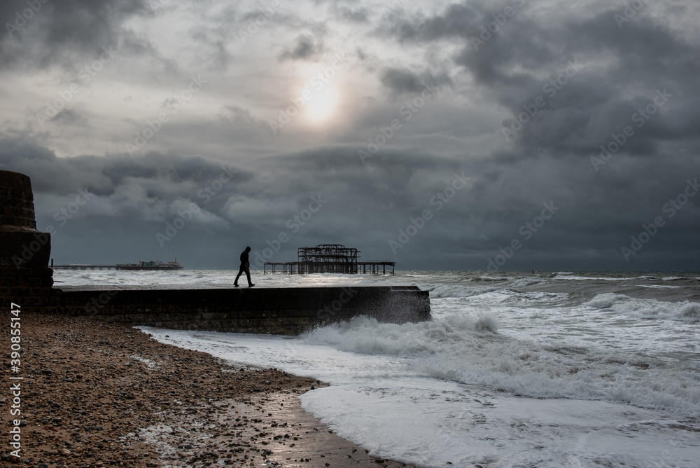 A man walking on groyne in Brighton during a stormy weather, UK