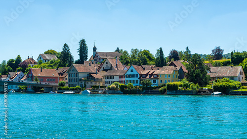 Petit village de maisons traditionnelles devant un lac en Suisse par une journée ensoleillée avec des arbres et de la verdure à l'arrière plan