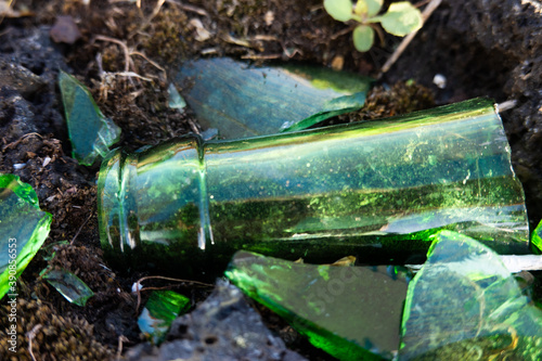 Close up of details of crushed emerald green glass bottles on black lava rock and soil, glistening in the sun, displaying a great pattern, a colour pallet, color scheme, reflexes, 
