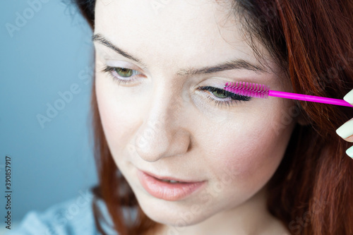 Red head woman brushing her extension eyelashes with a brush. girl with impending eyelid make-up mascara. Beauty industry. 