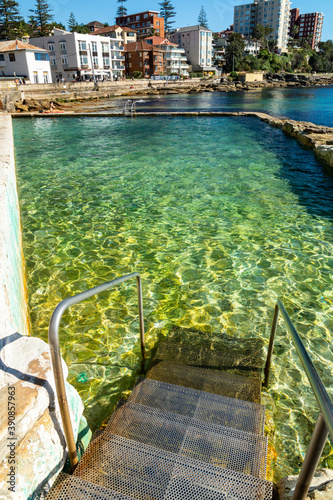 Metal stair going down in the transparent water of the rocky pool at Sydney Manly suburb with buildings on the background. Australia photo