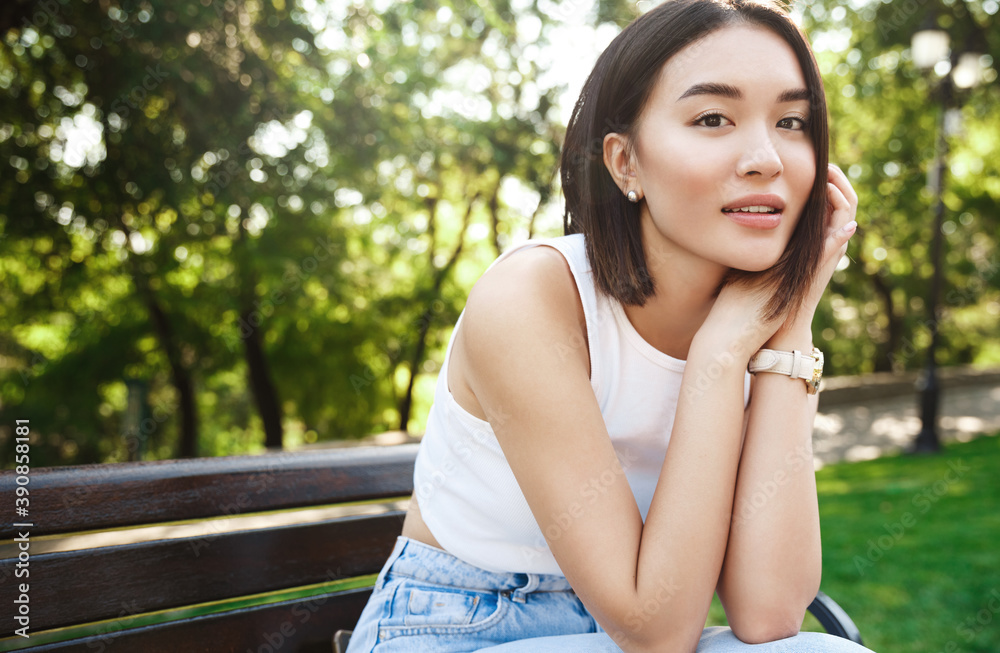 Outdoor shot of asian woman resting in park, sitting on bench and looking dreamy at camera. Concept of lifestyle and beauty Outdoor shot of asian woman resting in park, sitting on bench and looking dreamy at camera. Concept of lifestyle and beauty