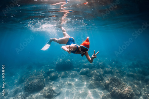Christmas holidays party with freediver. Happy freediver woman with New year cap glides underwater with fins in ocean. © artifirsov
