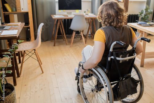 Back view of young brunette disable female in wheelchair moving towards table © pressmaster