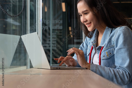 Young Asian woman wearing jeans jacket smiling. E - commerce business owner or freelance happy working use laptop Traveler blogger or remote work. Digital Nomad lifestyle.