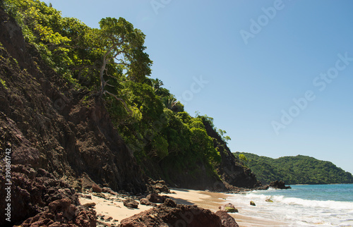 Beautiful landscape of the mexican pacific coast in a sunny day with trees, palms and green hills, some waves and cliffs with rocks