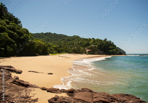 Beautiful landscape of the mexican pacific coast in a sunny day with a blue and clear sky, trees, palms and green hills, some waves and sand in the beach photo