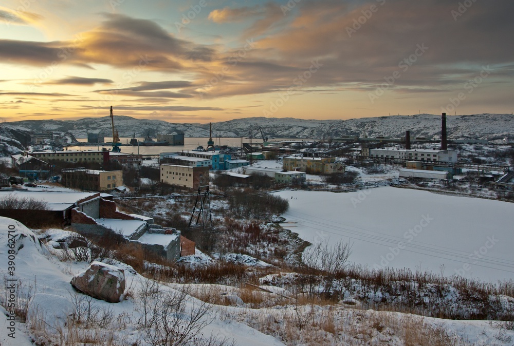 A view from top on Polyarny city in Russia: port, ships, houses and trees in winter. Sunset over hills.