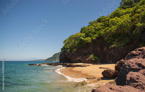 Beautiful landscape of a beach in the mexican pacific coast in a sunny day with a blue and clear sky, trees, palms and green hills, some waves and sand in the beach © Anthony J.
