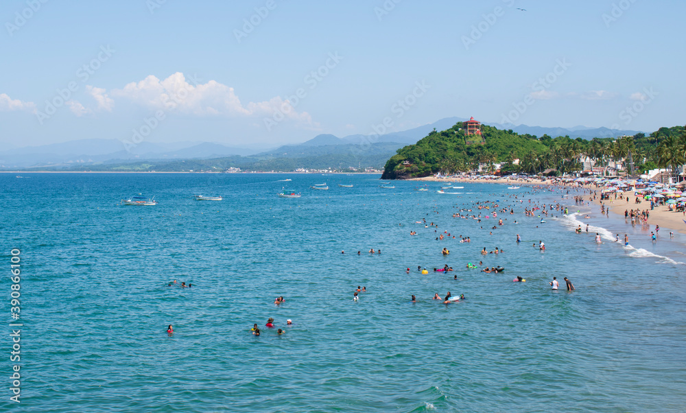 A lot of people taking vacations on a sunny and beautiful day in a mexican beach of the pacific coast with some green hills at the background