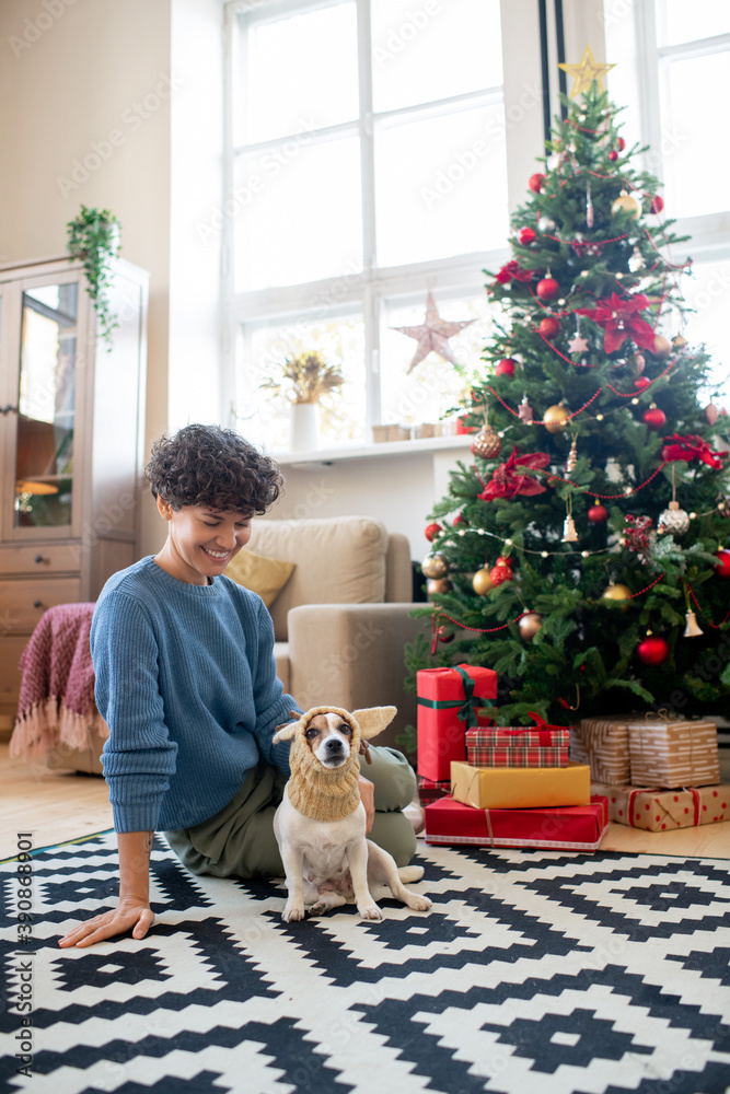 Obraz premium Young pretty female in casualwear looking at funny dog in knitted headwear