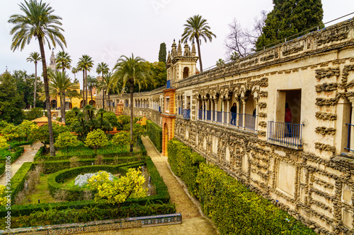 Jardín exterior de palacio andaluz en Sevilla con plantas ornamentales verdes y arquitectura árabe antigua con arcos y balcones.