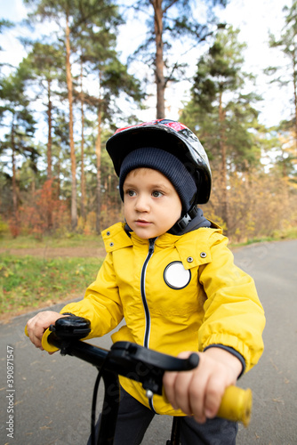 Active little boy in casual jacket and safety helmet riding his balance bicycle