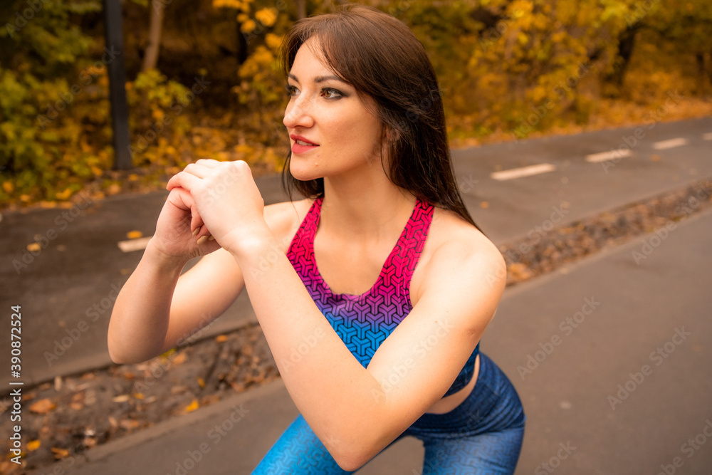 Portrait of fit young woman who doing squats. She training outdoors. Sportswoman wearing bright sportswear. Sport girl is smiling. Portrait of fit young woman who doing squats. She training outdoors. Sportswoman wearing bright sportswear. Sport girl is smiling.