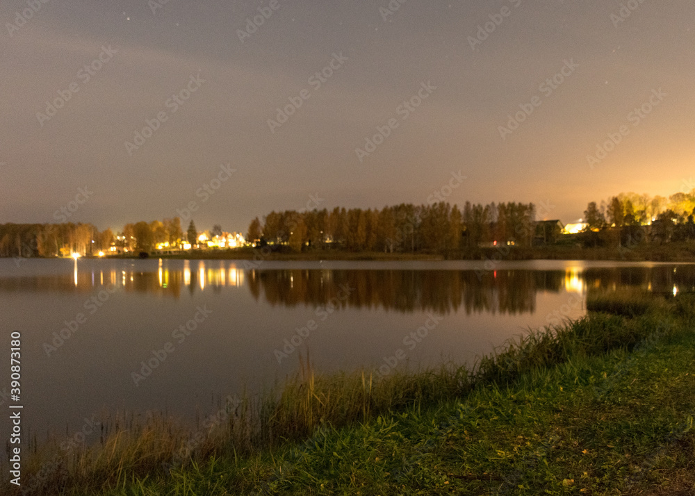 blurred wallpaper with lake at night, blurred lights on the horizon, lake reeds and grass in the foreground, autumn
